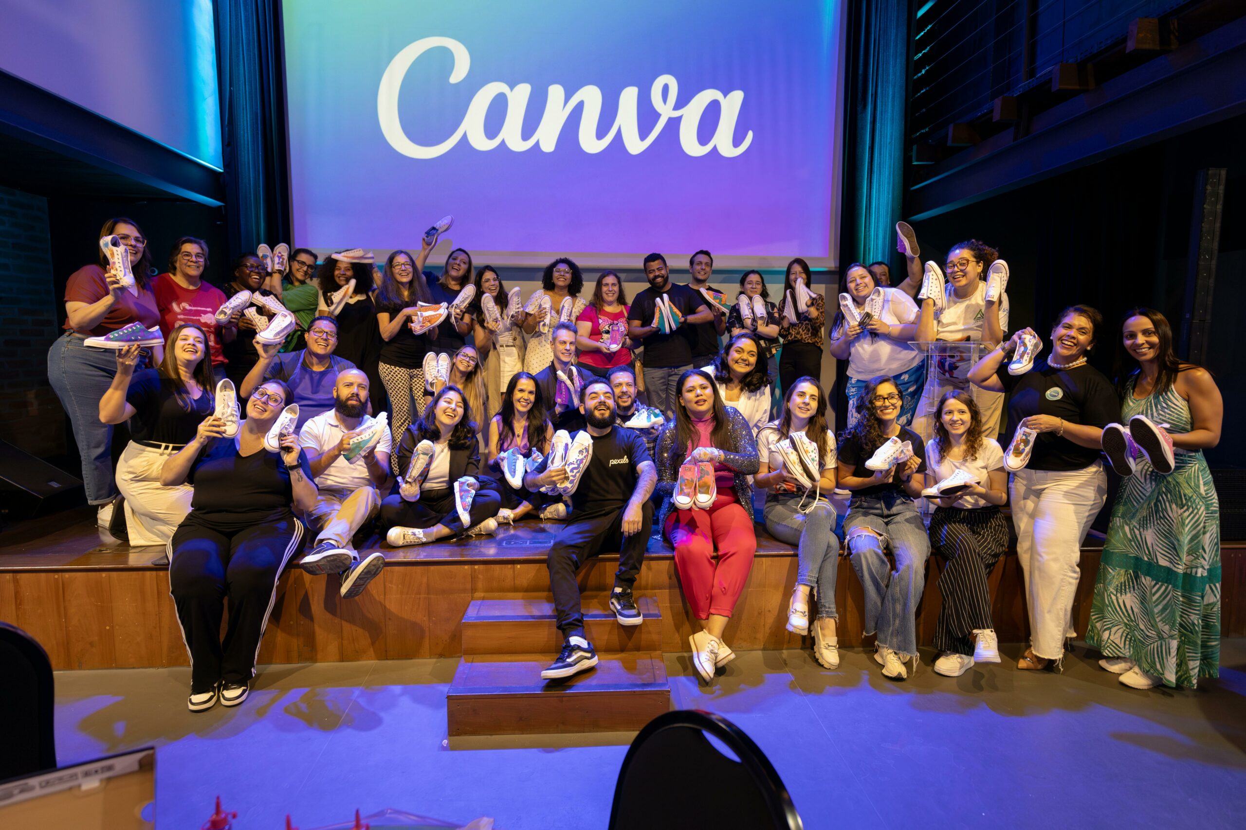 A diverse group of adults celebrating at a Canva event, holding sneakers on stage.
